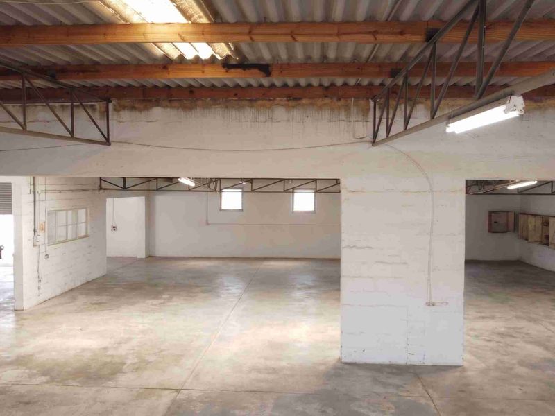 Spacious open-plan commercial utility area featuring exposed timber roof trusses, concrete flooring, and painted brick walls, suitable for storage or workshop use.