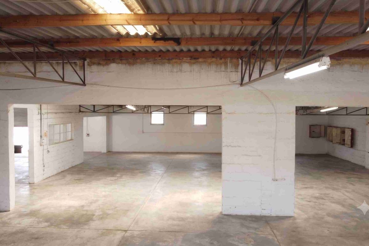 Spacious open-plan commercial utility area featuring exposed timber roof trusses, concrete flooring, and painted brick walls, suitable for storage or workshop use.