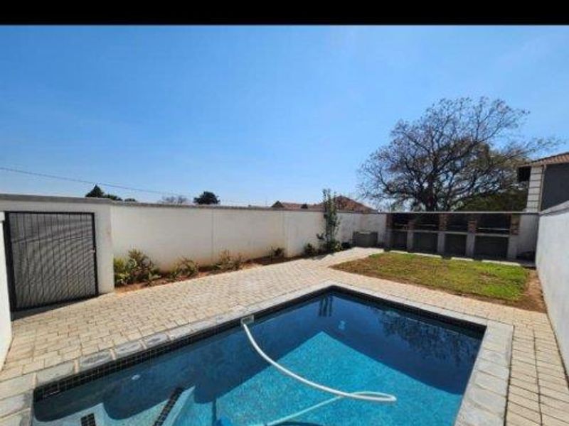Outdoor pool area featuring a swimming pool, paved patio, and a built-in braai area enclosed by a boundary wall.