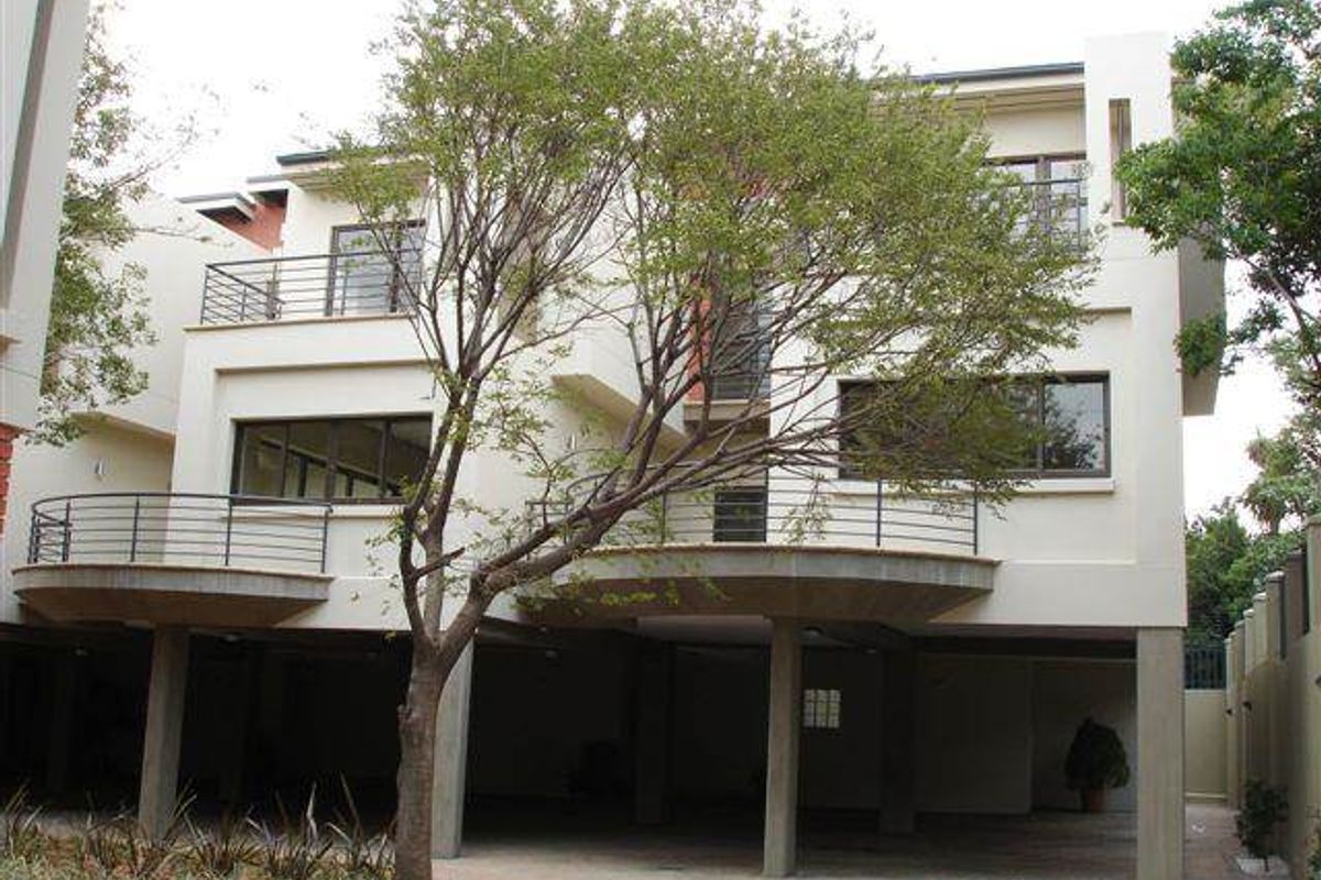 Rear elevation of a multi-story townhouse featuring elevated balconies with metal railings, large windows, and a covered ground-level parking area.