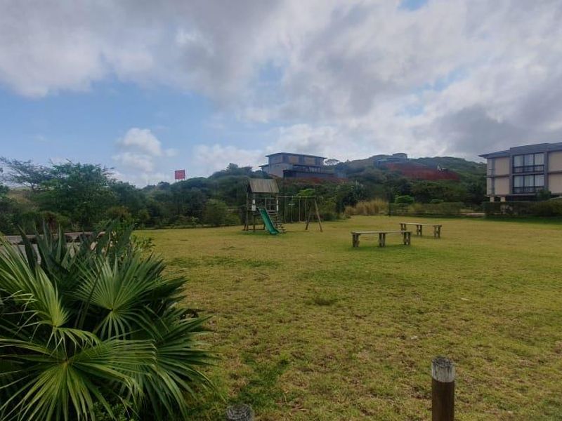 A spacious communal garden area featuring a well-maintained lawn, paved pathways, and timber bollards within a residential apartment complex setting.