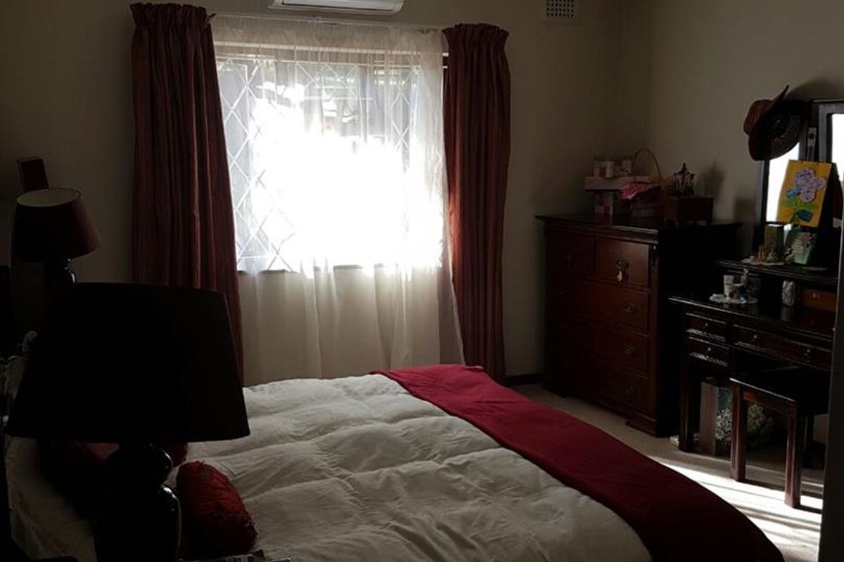 A functional bedroom featuring a split-system air conditioner, tiled ceiling, and security bars on the window.