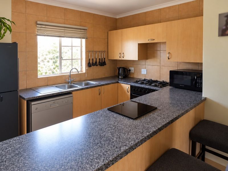 Functional kitchen featuring light wood cabinetry, granite-look laminate countertops, a breakfast bar, and tiled splashbacks with integrated gas hob and oven.