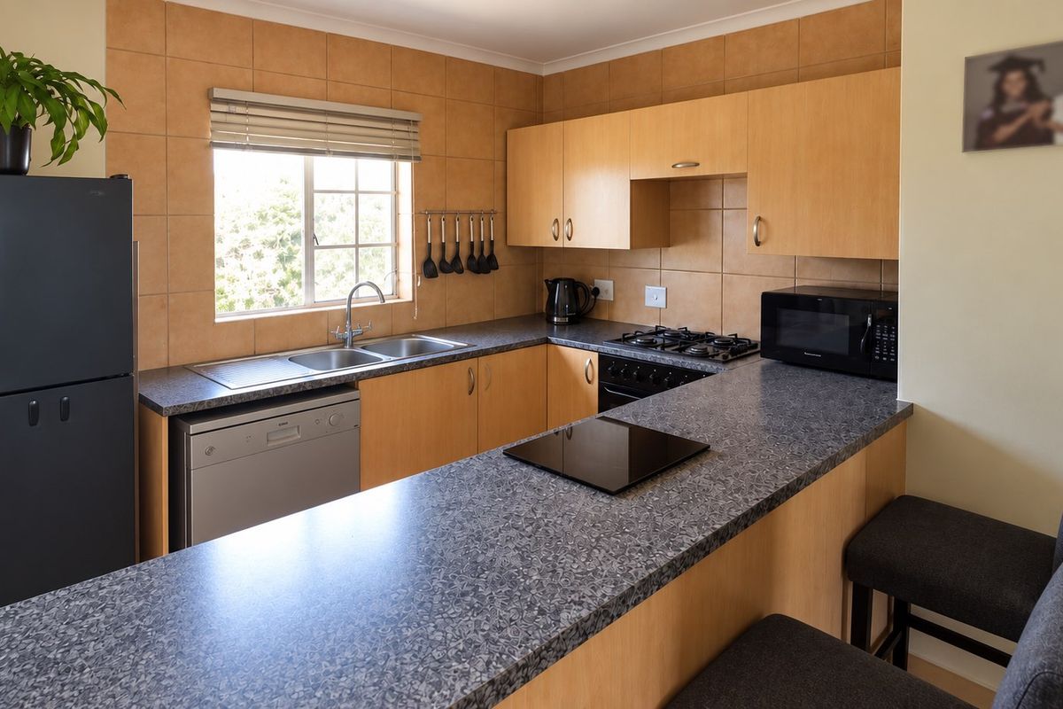 Functional kitchen featuring light wood cabinetry, granite-look laminate countertops, a breakfast bar, and tiled splashbacks with integrated gas hob and oven.