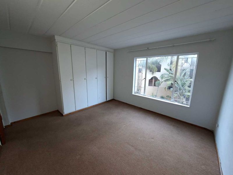 An empty bedroom featuring built-in cupboards, a large window with security bars, and carpeted flooring.