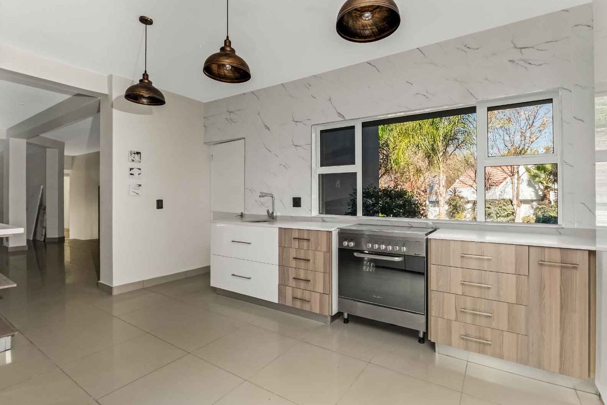 Modern kitchen featuring marble-look splashback, sleek two-tone cabinetry, stainless steel freestanding oven, and large window providing natural light and garden views.