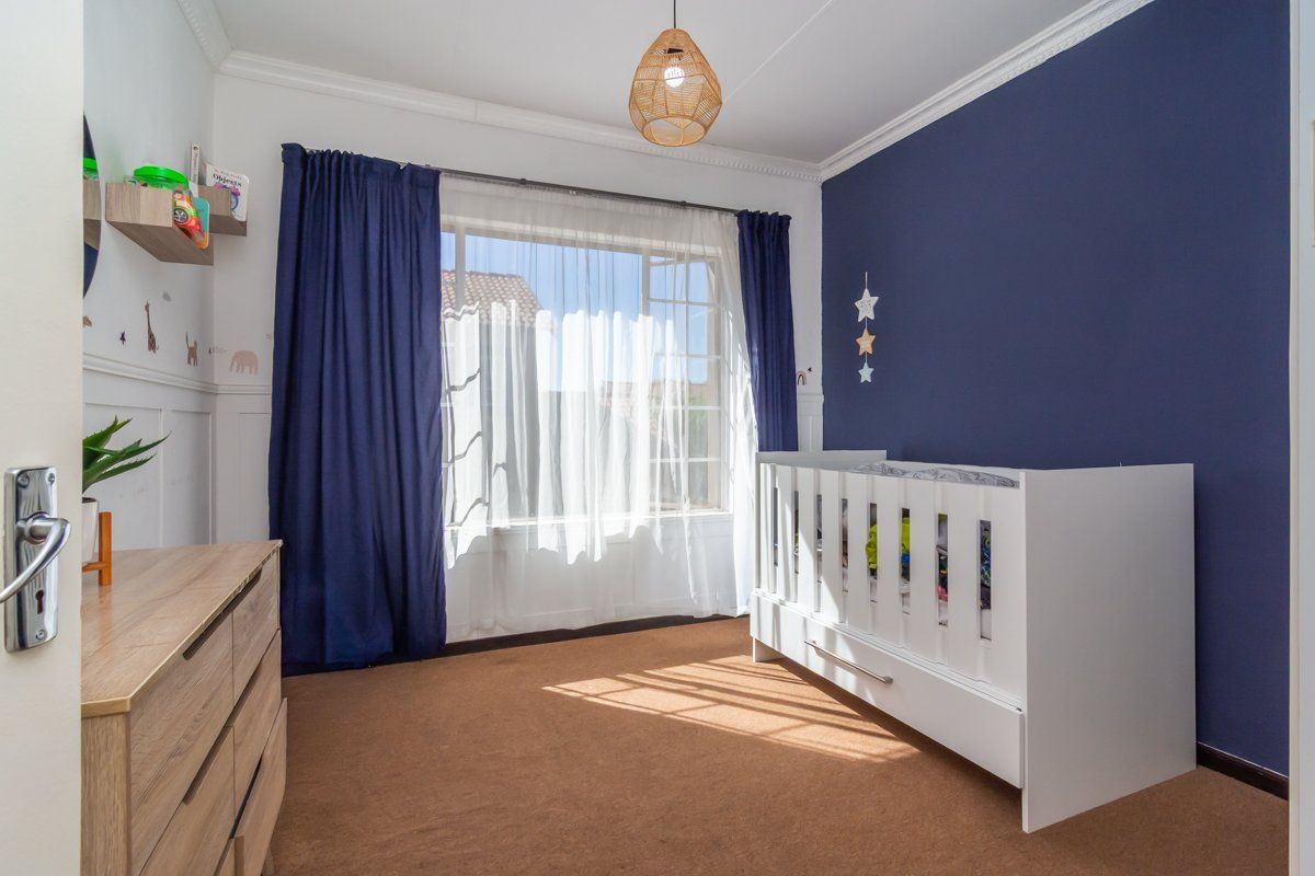 A well-lit bedroom featuring crown molding, wainscoting, and a large window with natural light, finished with carpet flooring.