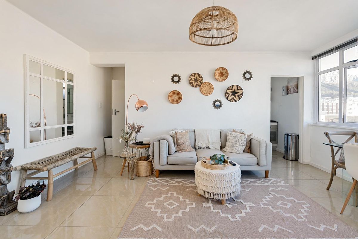 A bright and well-maintained living room featuring neutral tiled flooring, clean white walls, and large windows allowing for ample natural light.