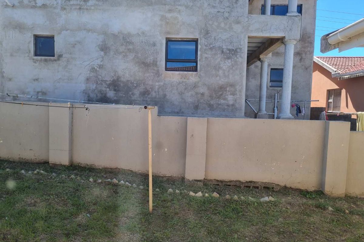 Rear view of a multi-story residential property featuring an unfinished concrete facade, perimeter boundary wall, and a small garden area.
