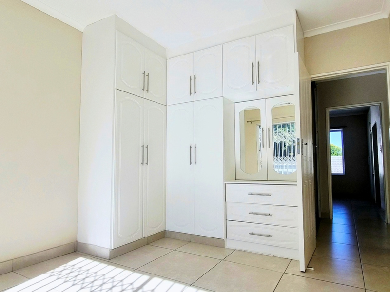 A bright bedroom featuring ample built-in cupboard storage, integrated vanity drawers, and neutral tiled flooring throughout.
