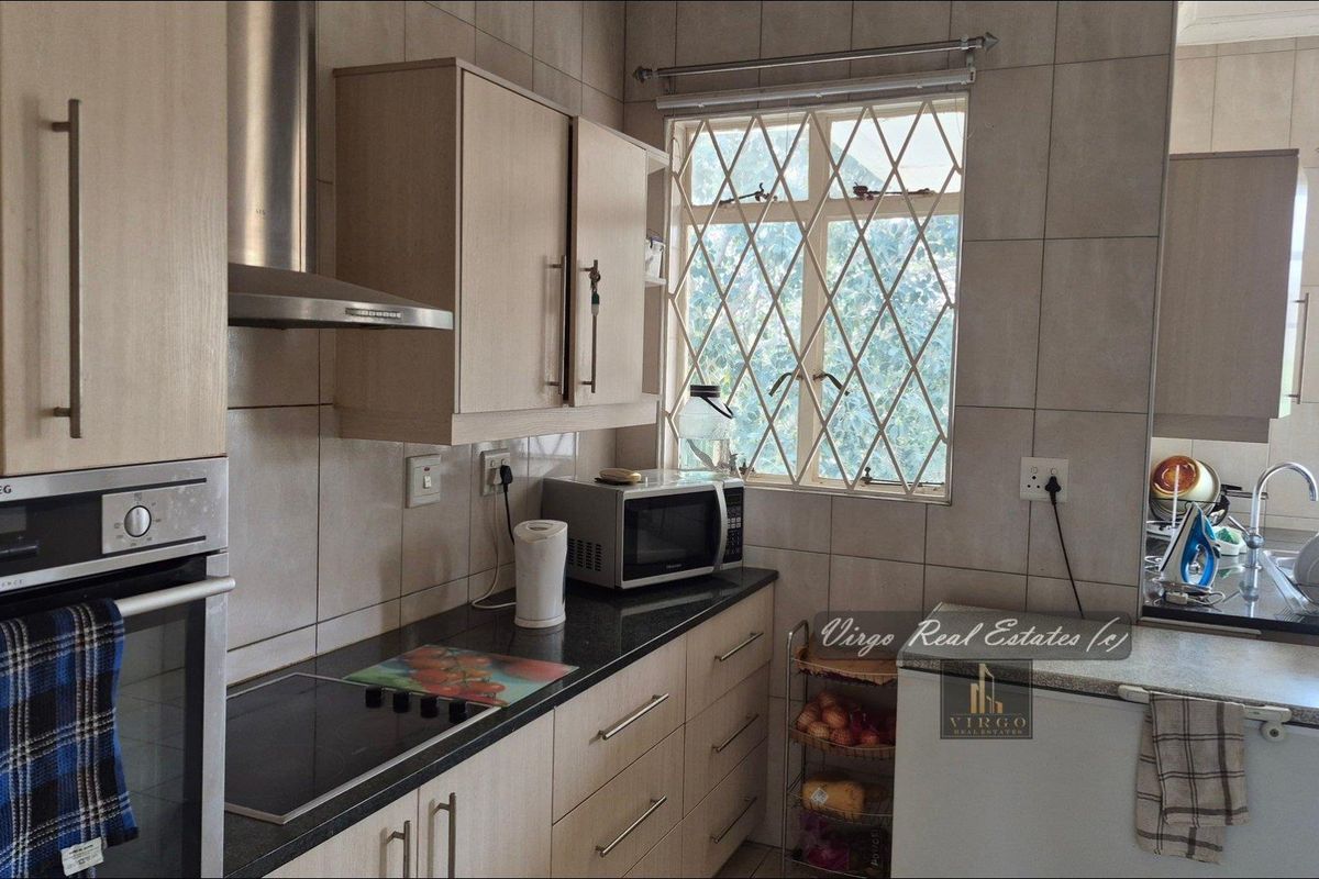 A functional kitchen featuring built-in cabinetry, granite countertops, a modern oven, and a hob, complemented by tiled walls and security bars on the windows.