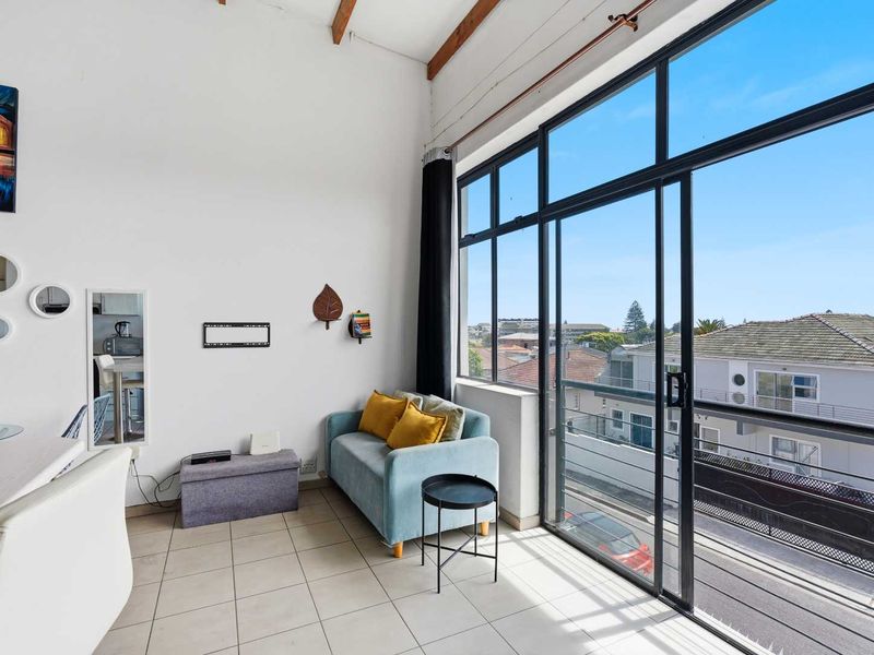Bright living area featuring high ceilings with exposed timber beams, tiled flooring, and large sliding glass doors opening to a balcony with neighborhood views.