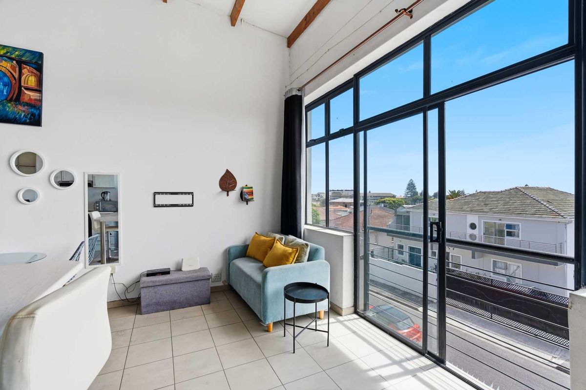 Bright living area featuring high ceilings with exposed timber beams, tiled flooring, and large sliding glass doors opening to a balcony with neighborhood views.