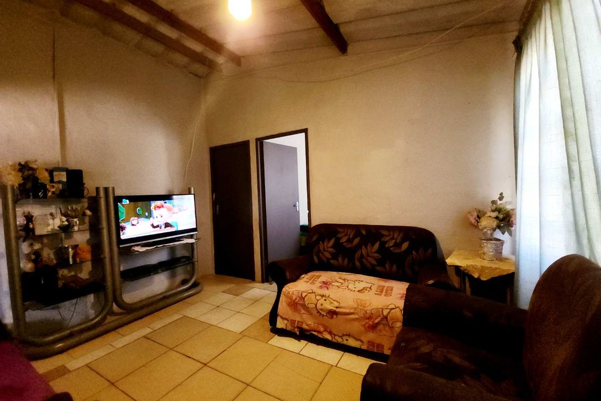 A living room featuring tiled flooring, exposed ceiling beams, and direct access to an adjacent room.