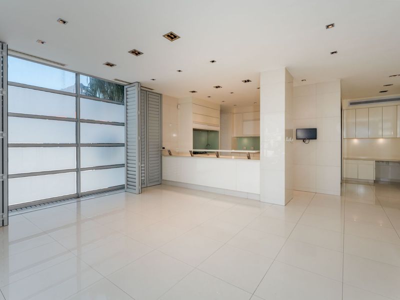 Spacious open-plan living and kitchen area featuring high-gloss tiled floors, modern built-in cabinetry, and large glass folding doors leading to the exterior.