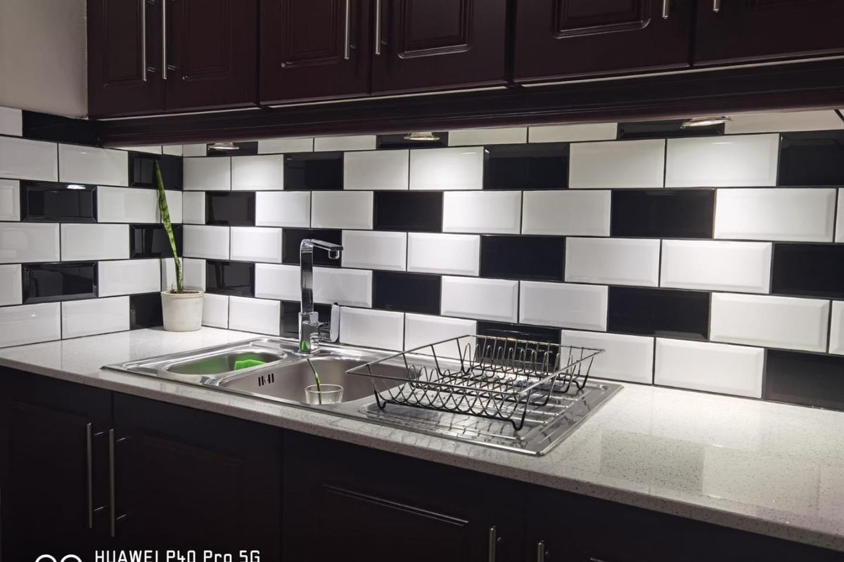 A kitchen workspace featuring dark wood cabinetry, a contrasting black and white subway tile backsplash, and a stainless steel sink with stone countertops.
