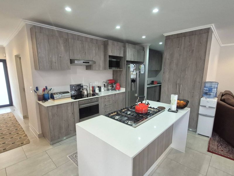 Modern open-plan kitchen featuring wood-finish cabinetry, a central island with a gas hob, and integrated appliances, seamlessly flowing into the living area.