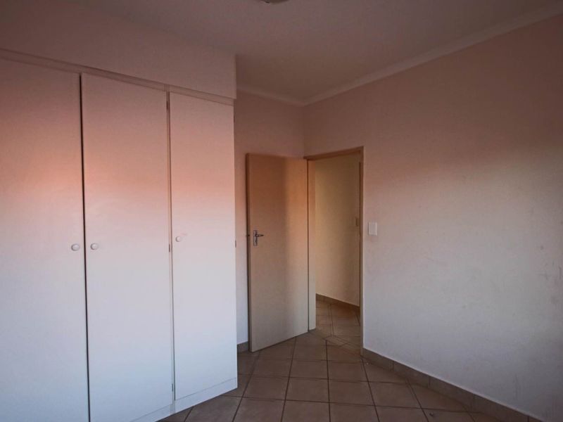 An empty bedroom featuring built-in cupboards and tiled flooring, offering a clean and neutral space ready for personalization.