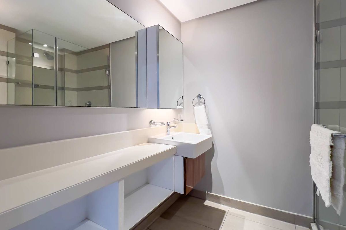 Modern bathroom featuring a wall-mounted vanity with integrated basin, large mirror, and a glass-enclosed shower area with neutral tiling.