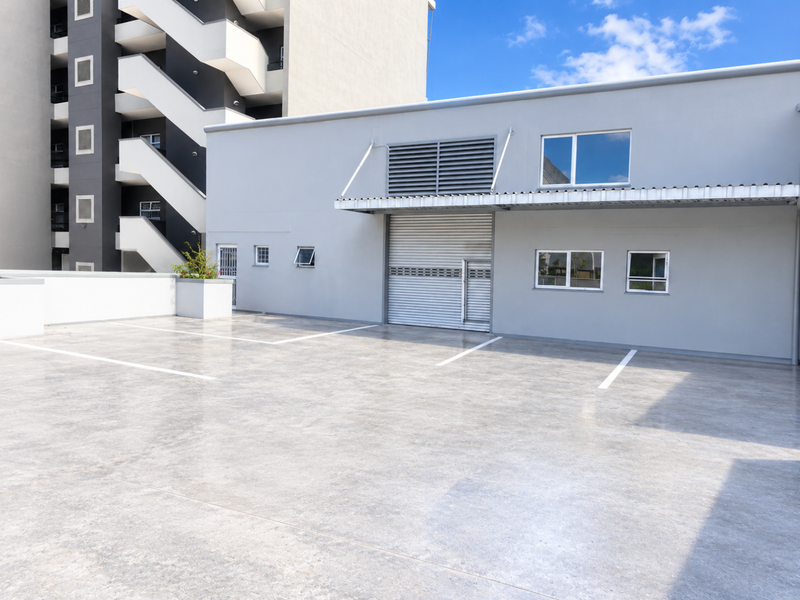 A clean, modern exterior rear view featuring a paved parking area, a large roller shutter door, and a metal awning on a well-maintained building.