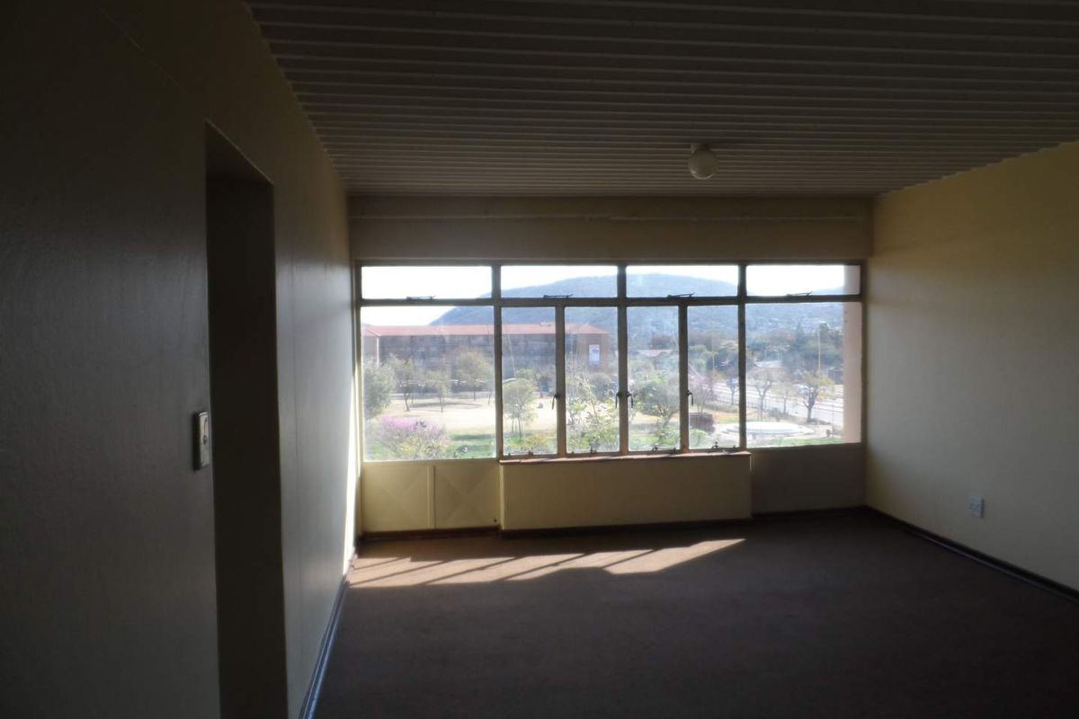 An empty living room featuring large windows with natural light, carpeted flooring, and a corrugated ceiling finish.