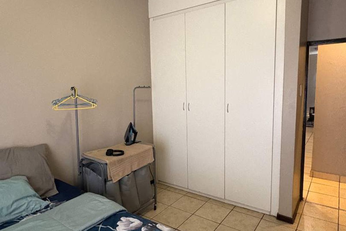 A bedroom featuring built-in cupboards, tiled flooring, and a coved ceiling, providing a functional and neutral living space.