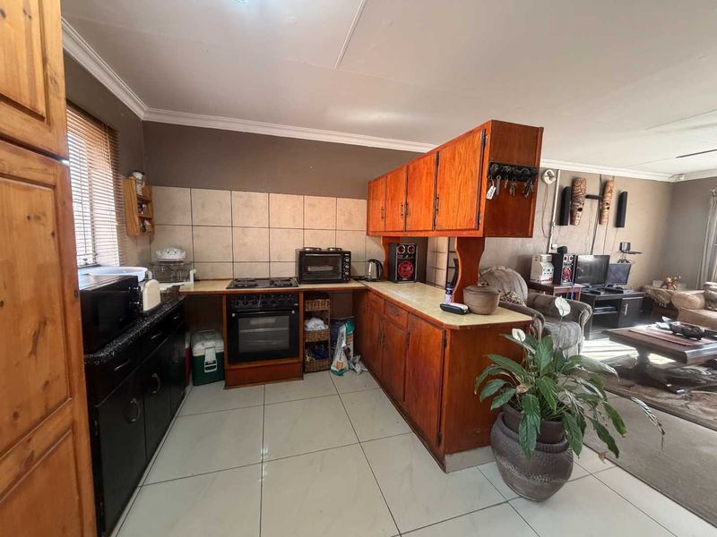 Open-plan kitchen featuring built-in wooden cabinetry, tiled flooring, and a functional layout that flows into the adjacent living area.