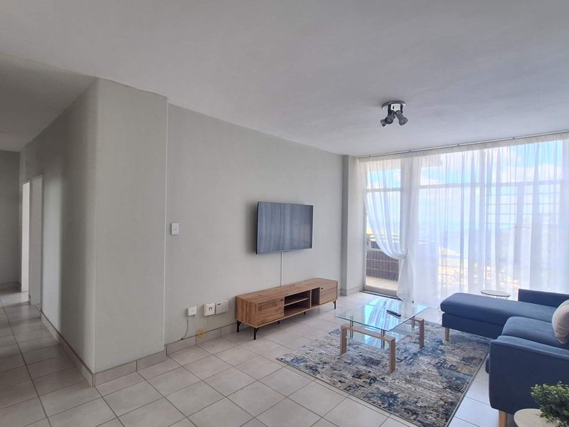 A bright and spacious living room featuring tiled flooring and a large sliding glass door that provides ample natural light.