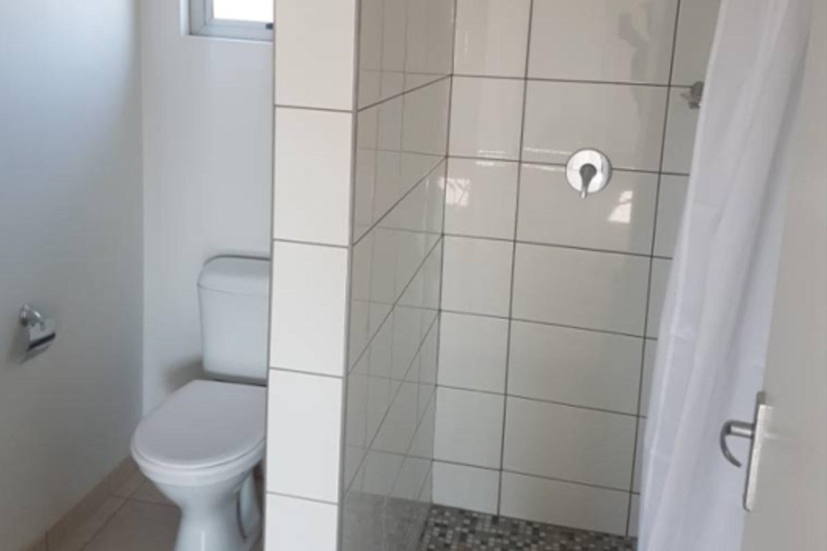 A functional bathroom featuring a tiled shower enclosure with mosaic flooring, a standard toilet, and a window for natural light.