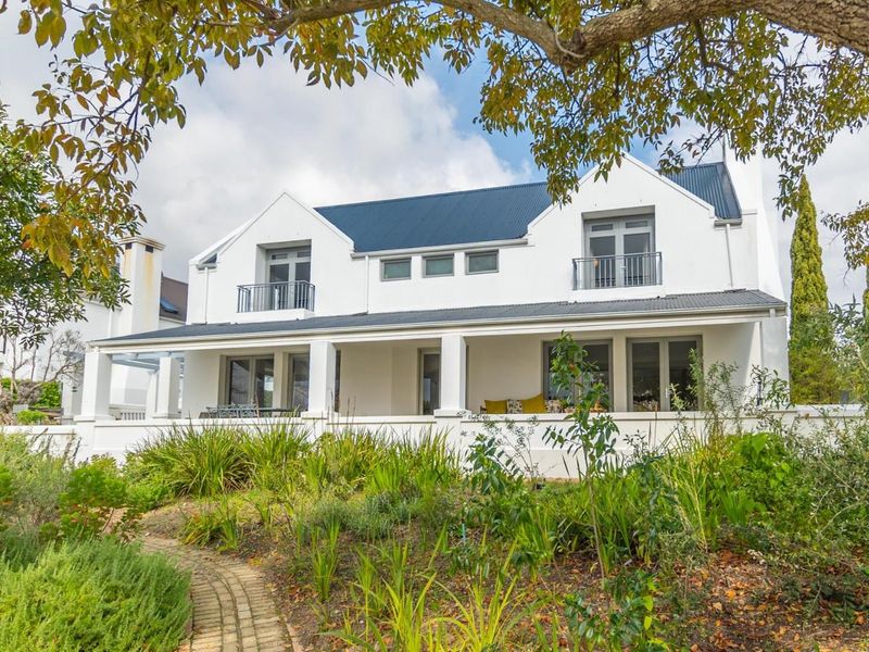 A well-maintained double-story residence featuring a covered patio, upper-level balconies, a corrugated metal roof, and a landscaped garden with a brick pathway.