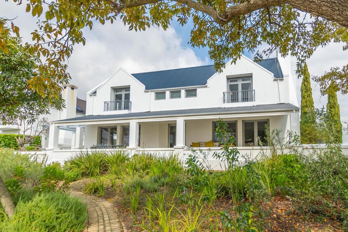 A well-maintained double-story residence featuring a covered patio, upper-level balconies, a corrugated metal roof, and a landscaped garden with a brick pathway.