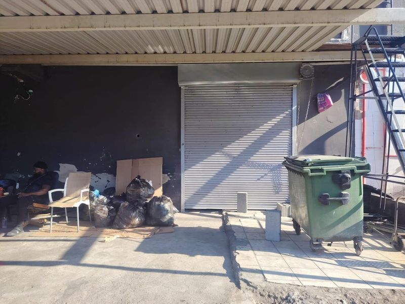 Rear exterior area of an industrial property featuring a metal roller shutter door, covered canopy, and external staircase access.