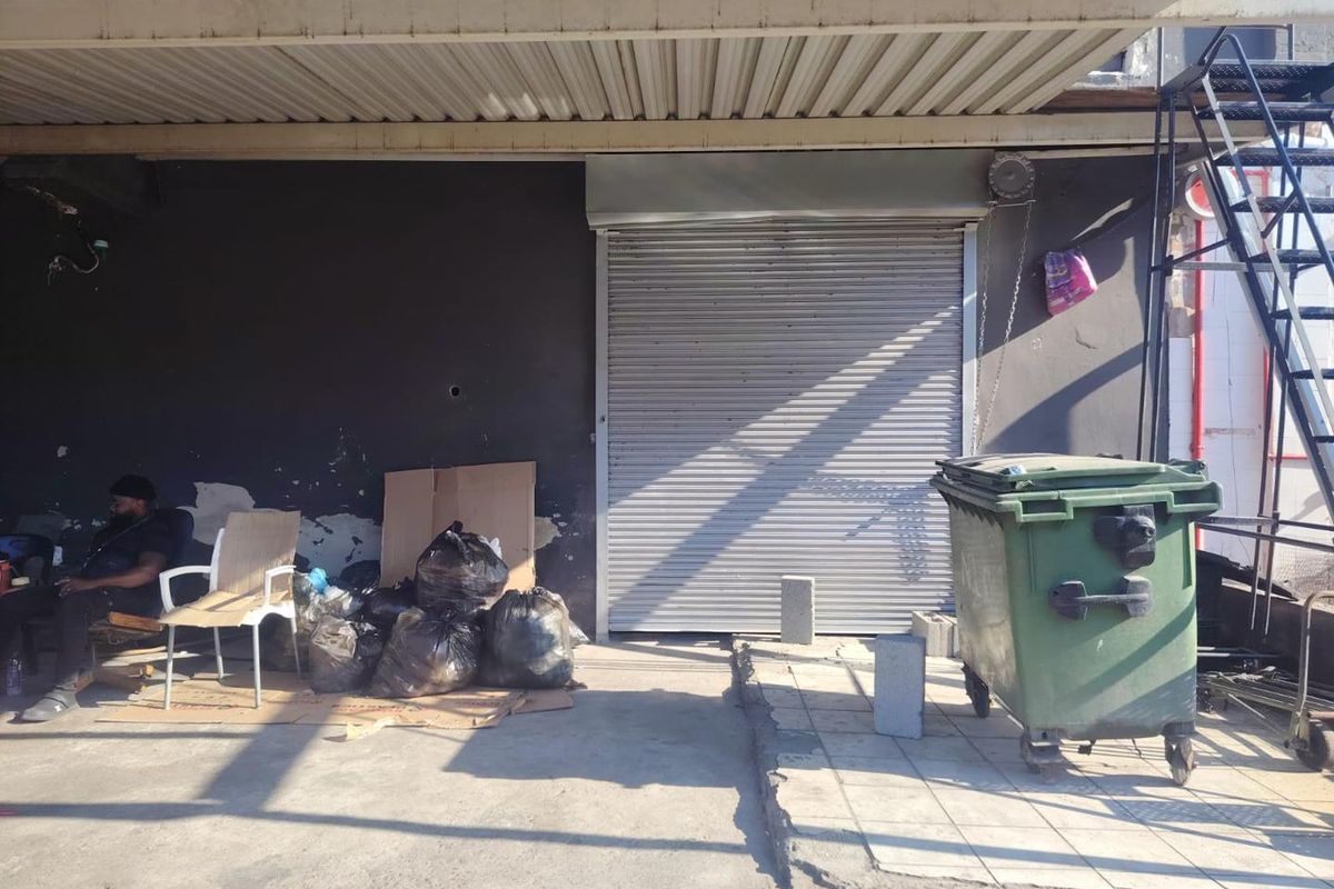 Rear exterior area of an industrial property featuring a metal roller shutter door, covered canopy, and external staircase access.