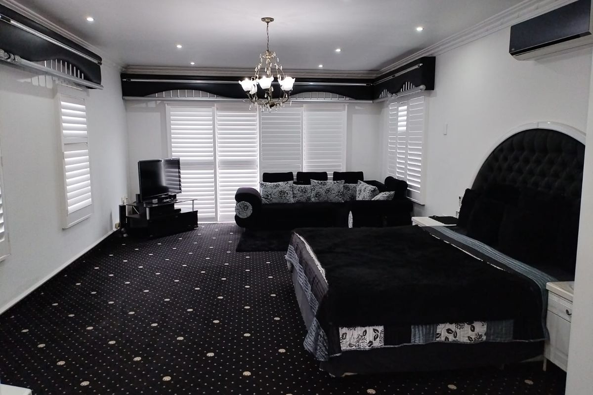 Spacious bedroom featuring recessed downlights, a central chandelier, plantation shutters, and a wall-mounted air conditioning unit.