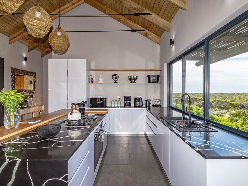 Modern kitchen featuring high-end marble-effect countertops, sleek cabinetry, and an exposed timber vaulted ceiling with expansive views of the surrounding landscape.