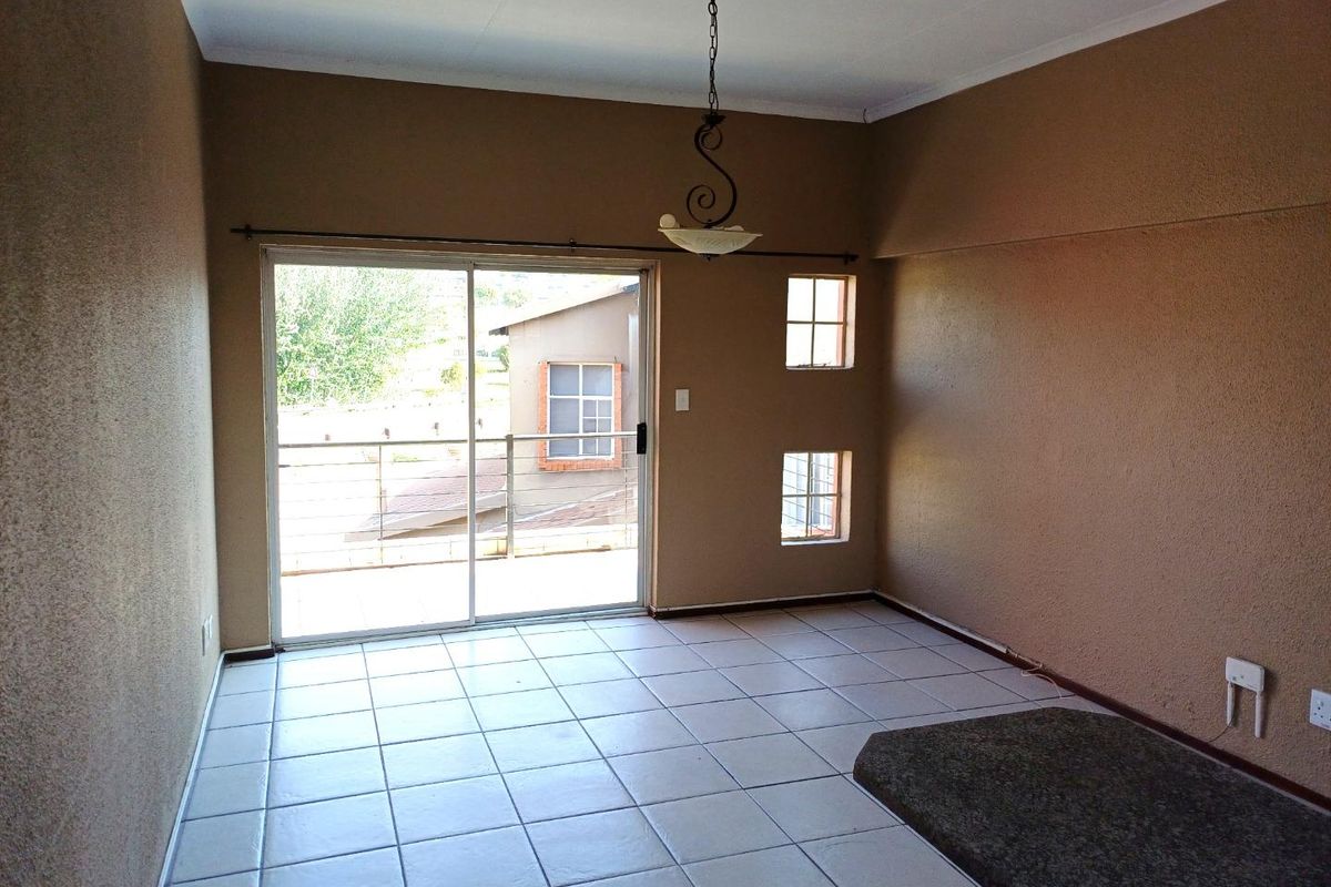 An empty living area featuring tiled floors, a granite breakfast bar, a pendant light, and a sliding door leading to an outdoor balcony.
