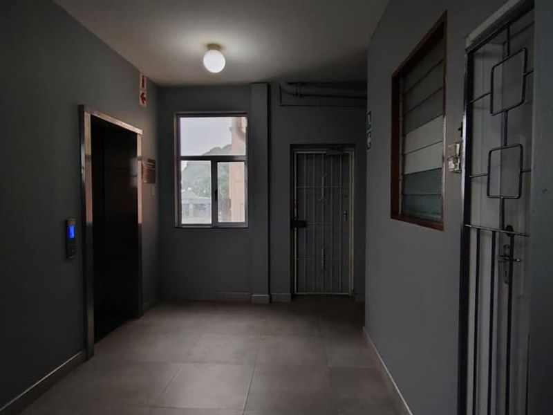A clean, modern commercial hallway featuring tiled flooring, an elevator access point, and a secure metal gate.