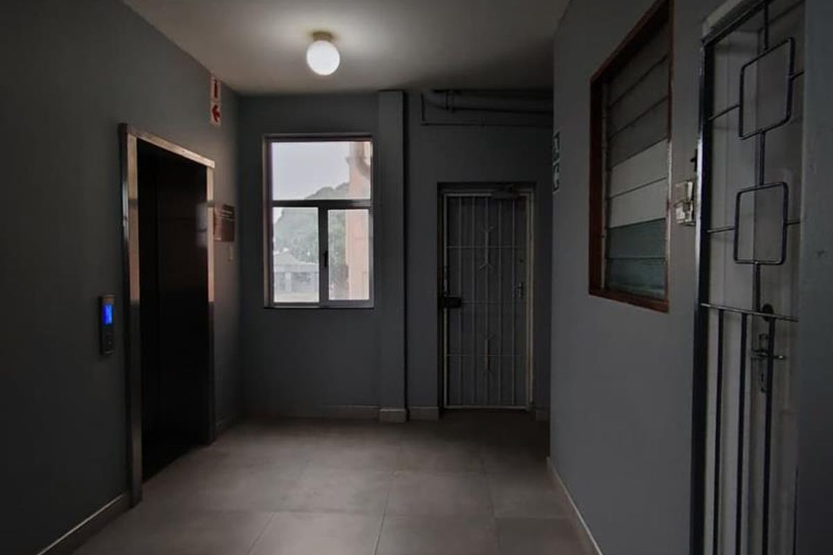A clean, modern commercial hallway featuring tiled flooring, an elevator access point, and a secure metal gate.
