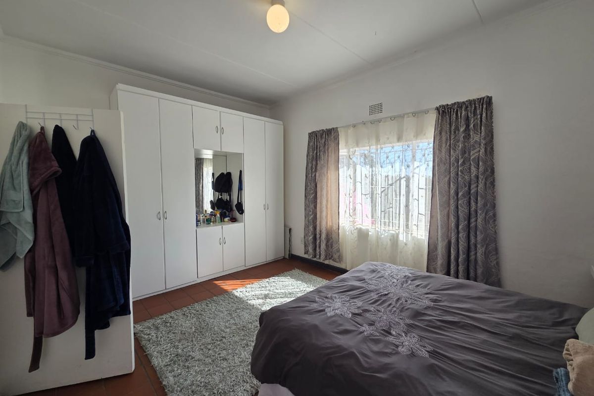 A bedroom featuring built-in cupboards with a central mirror, tiled flooring, and a window fitted with security bars.