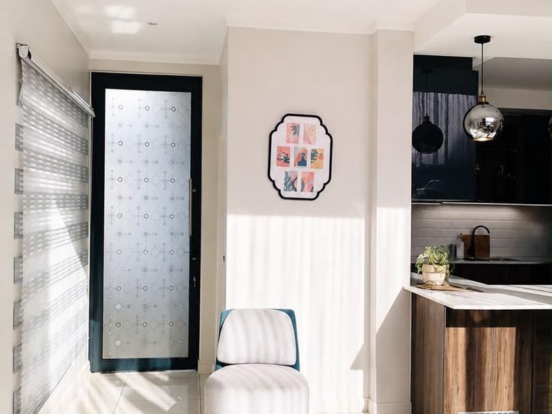 A bright open-plan living area featuring modern tiled flooring, a sleek kitchen island with built-in cabinetry, and a stylish frosted glass entrance door.