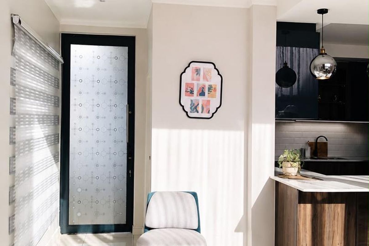 A bright open-plan living area featuring modern tiled flooring, a sleek kitchen island with built-in cabinetry, and a stylish frosted glass entrance door.