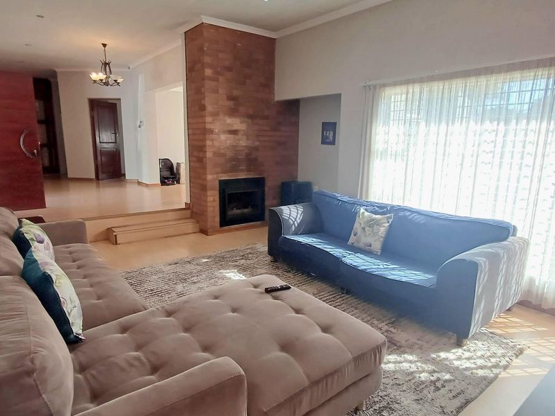 Spacious living room featuring a prominent brick fireplace, raised platform area, and large windows allowing for ample natural light.