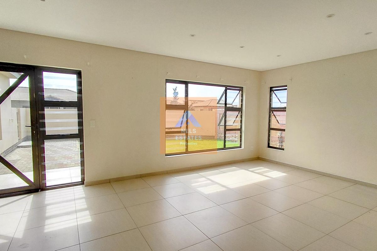 A bright, empty living area featuring neutral tiled flooring, modern aluminium window frames, and recessed downlighting, offering a clean canvas for interior design.