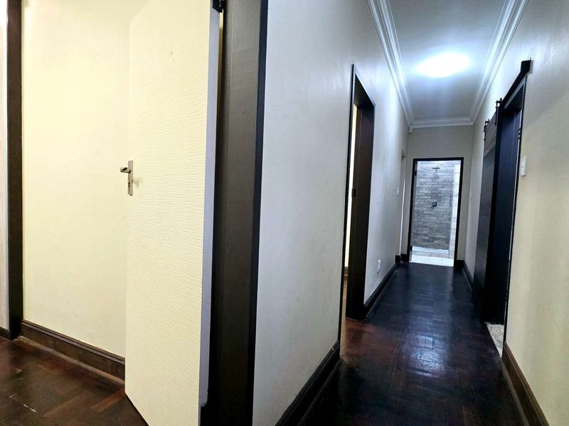 A well-maintained hallway featuring dark parquet flooring, contrasting door frames, and coving, leading towards a tiled bathroom area.