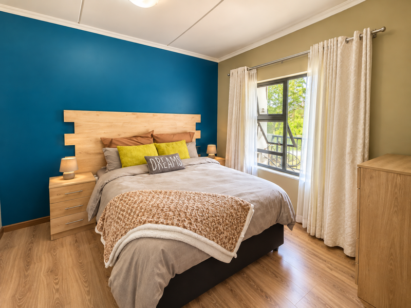 A well-maintained bedroom featuring laminate flooring, a large window with curtain rod, and a blue accent wall.