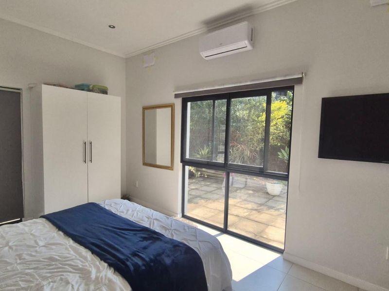 A bright bedroom featuring tiled flooring, a split-system air conditioner, and a sliding glass door providing direct access to the outdoor patio area.