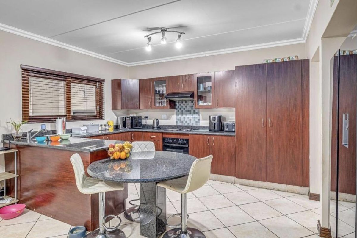 A functional kitchen featuring dark wood cabinetry, granite countertops, a built-in oven with extractor fan, and a breakfast nook with a stone-topped table.