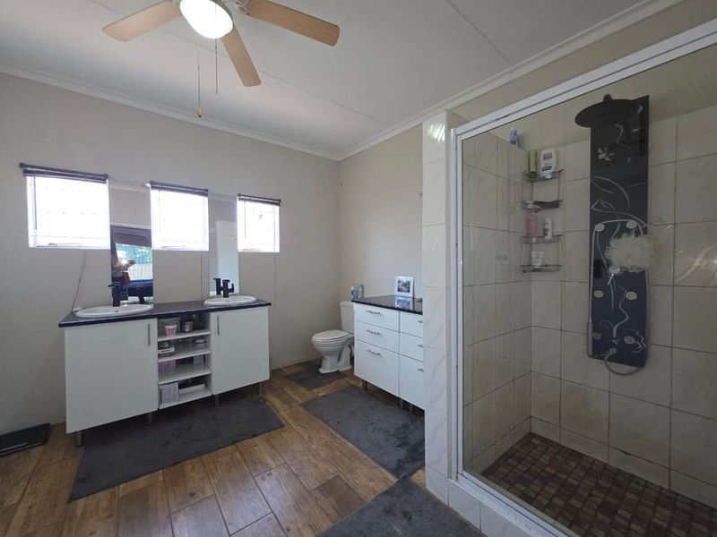 A spacious bathroom featuring a double vanity with storage, a separate shower enclosure with a modern panel, and tiled flooring.
