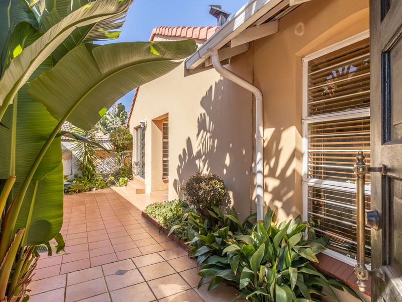 A well-maintained tiled patio area featuring established garden beds, guttering, and access to the home through a timber door.