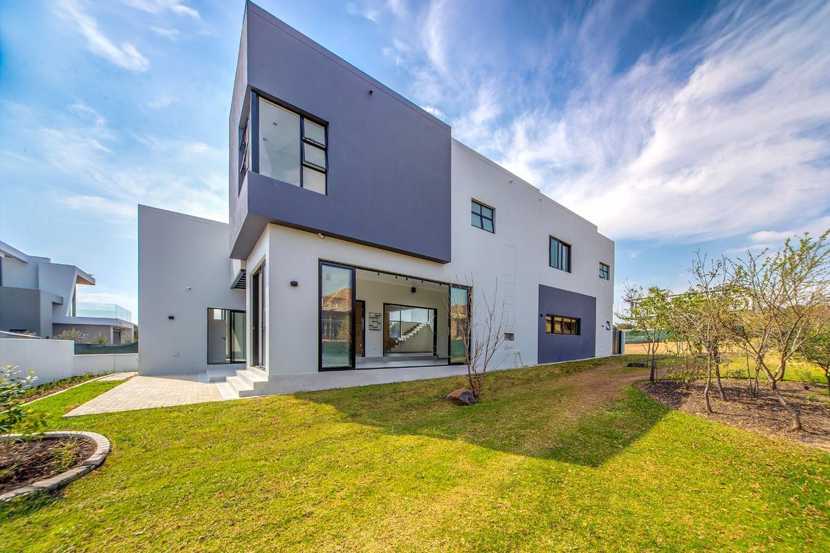 Modern rear elevation of a contemporary home featuring large sliding glass doors, a paved patio area, and a well-maintained garden.